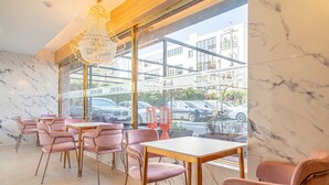 Een modern interieur met marmeren wanden, roze stoelen en een groot raam met uitzicht op een parkeerplaats.