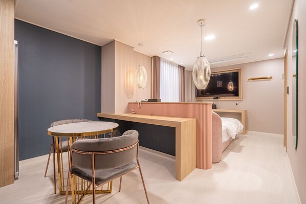 A modern hotel room with a dining area, a bed, and a small kitchenette.