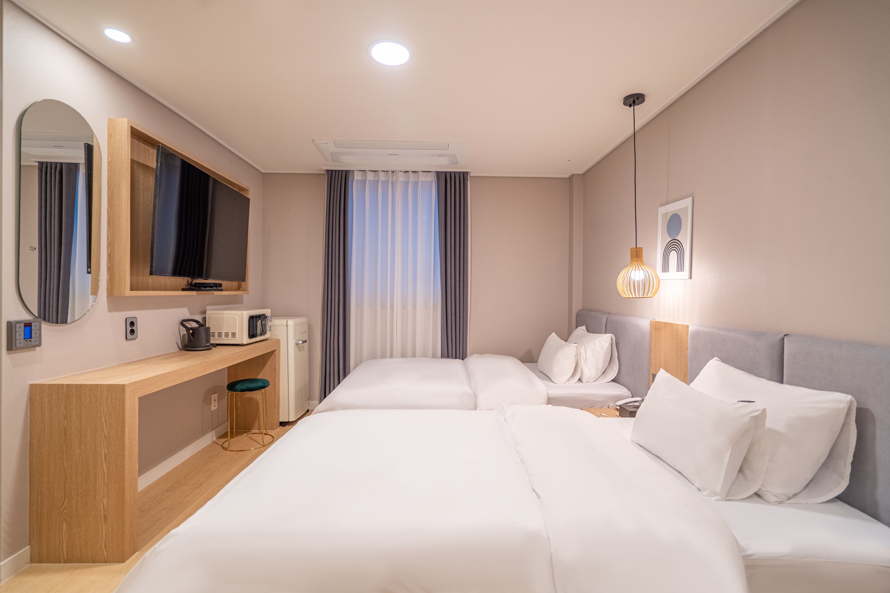 A modern hotel room with a large bed, a desk with a microwave, a TV, and a bedside table with a lamp.