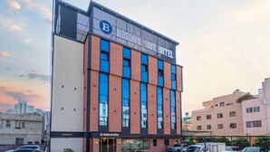 Een modern hotelgebouw met een opvallend ‘B’ logo op de gevel, grote ramen en een parkeerplaats met verschillende auto's.