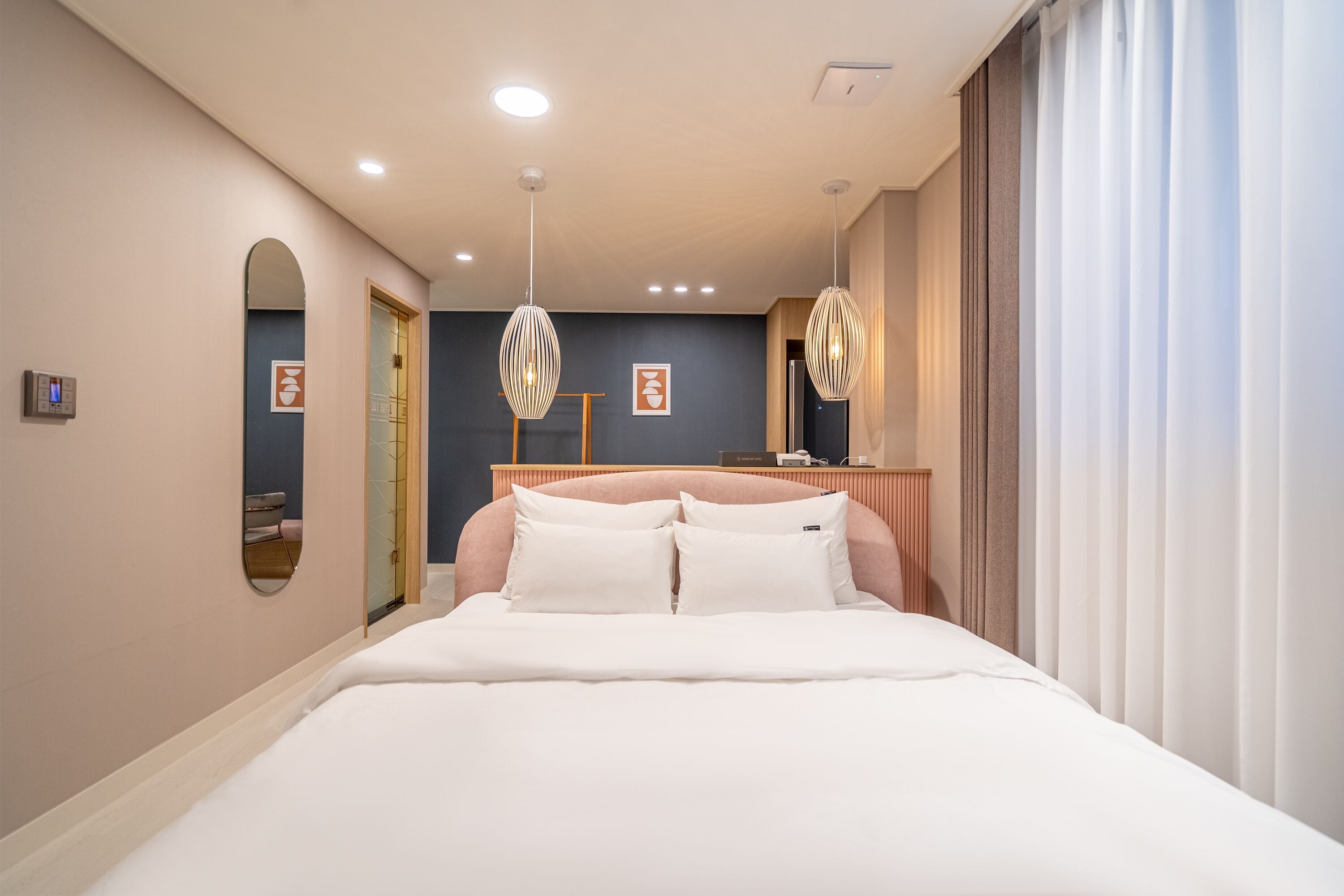 A modern hotel room with a large bed, two bedside tables, a mirror, and a ceiling light fixture.