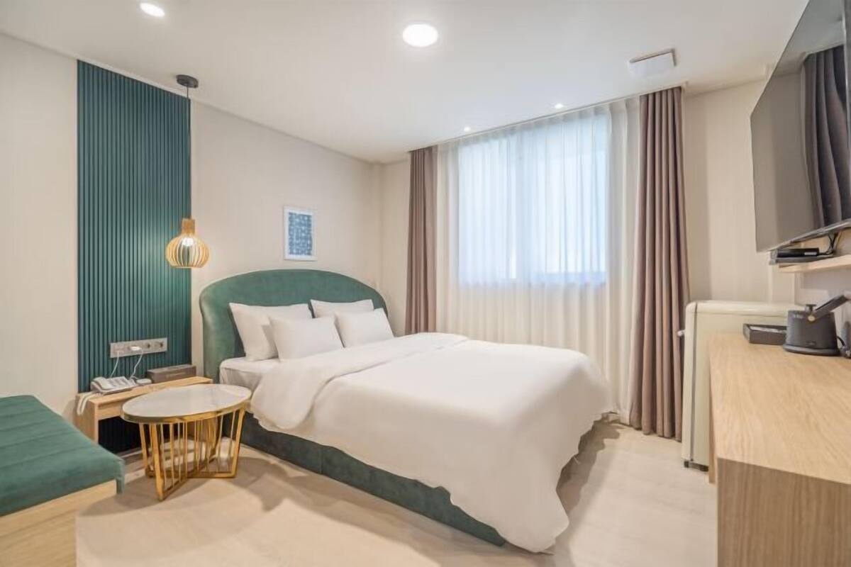 Habitación de hotel con cama, escritorio, silla, mesa redonda, televisor y ventana con cortinas.