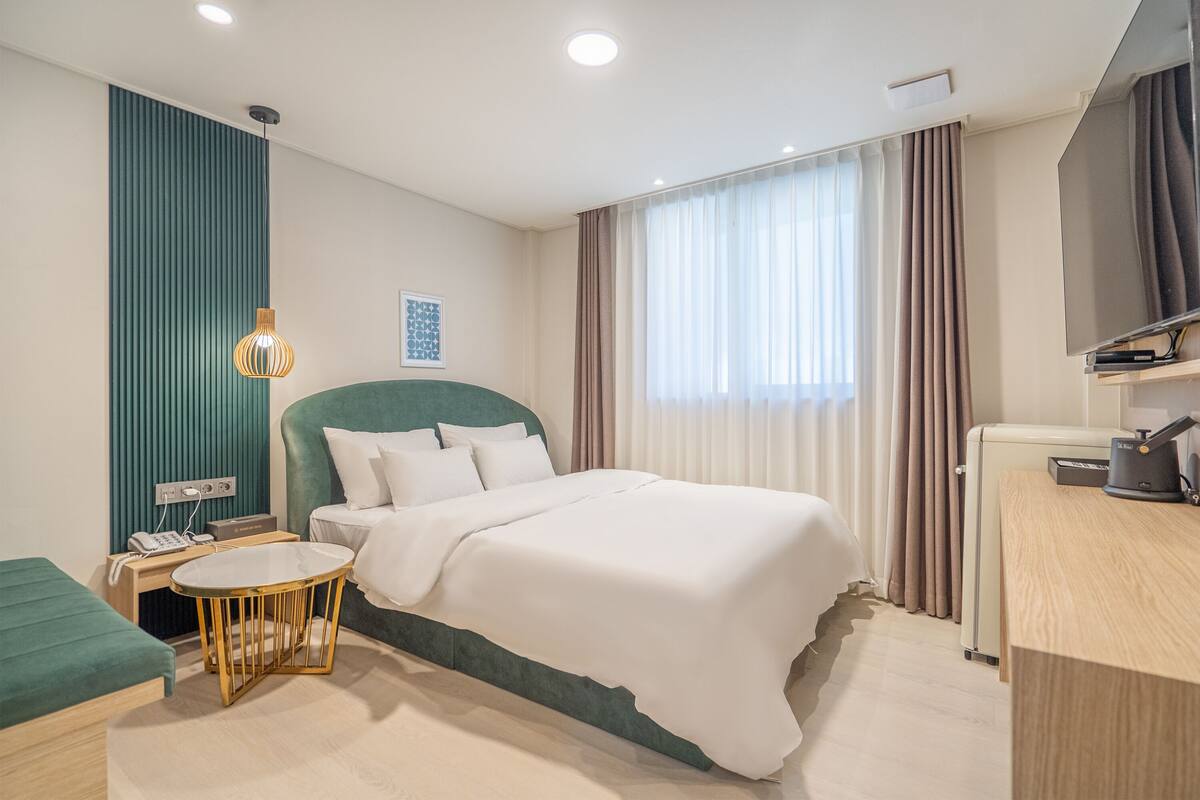 Una habitación de hotel moderna con cama, escritorio, silla, televisor y ventana con cortinas.