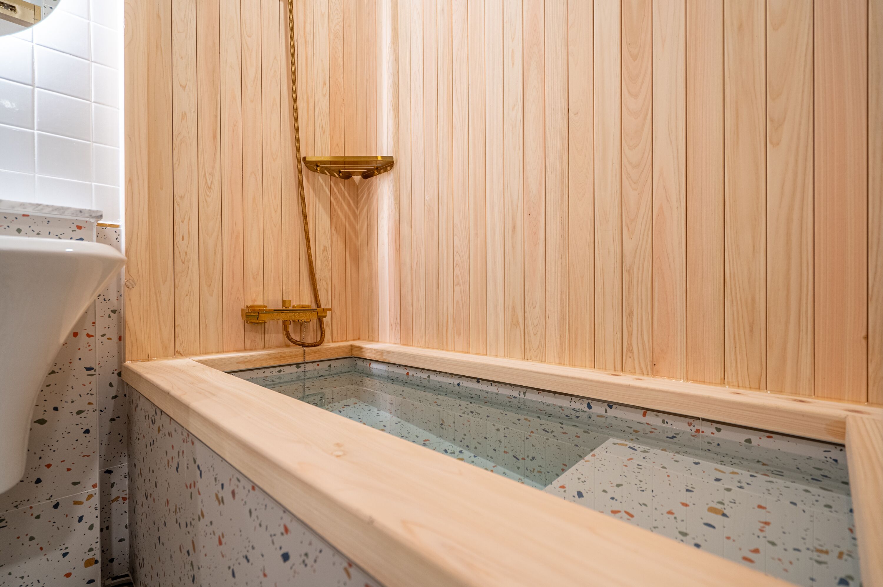 A wooden sauna with a glass floor, a gold showerhead, and a white bathtub in the corner.