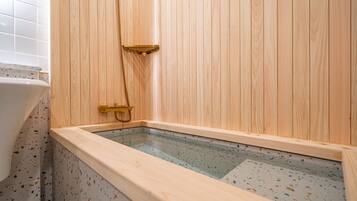 A wooden sauna with a glass floor, a gold showerhead, and a white bathtub in the corner.