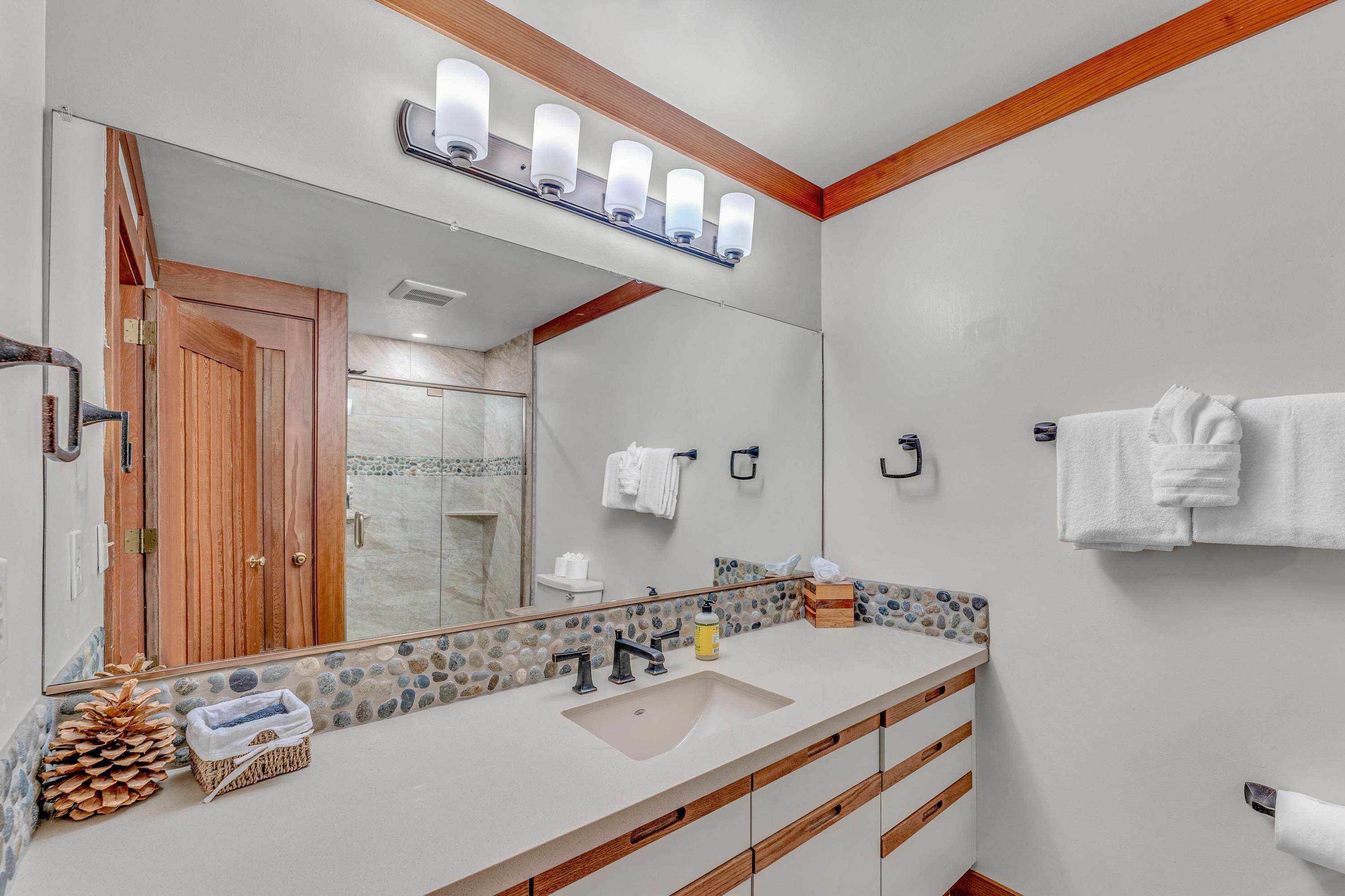 A bathroom with a large mirror, wooden vanity, white sink, and a towel rack.