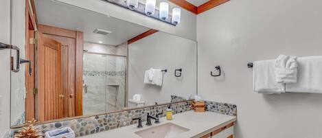 A bathroom with a large mirror, wooden vanity, white sink, and a towel rack.