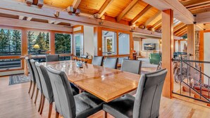 Un comedor amplio con una mesa y sillas de madera, ventanas grandes y vistas a árboles.