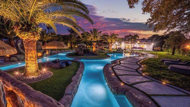 A pool area with a winding water feature, palm trees, and stone pathways. - One and Only Lazy River Pool Villa (Miami)