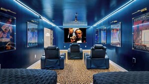 A home theater room with dark blue walls, a large screen, and three reclining chairs. - One and Only Lazy River Pool Villa (Miami)