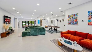 A modern living room with a green sectional sofa, a red sofa, and a white coffee table. There are two paintings on the walls and a bench in the center. - One and Only Lazy River Pool Villa (Miami)