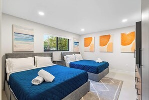 Two large beds with matching nightstands and tables, complemented by abstract artwork and a wardrobe with mirror.