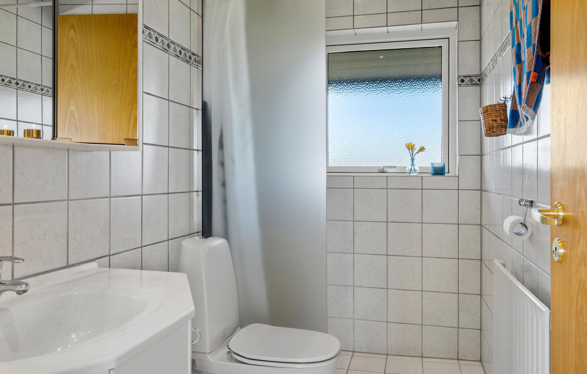 Un baño con lavamanos, inodoro y cortina de ducha blanca. Se ve una ventana con vista al mar.