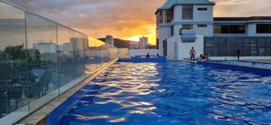 A rooftop swimming pool with a glass barrier, a building with a sign reading "HOTEL PHOENIX," and a sunset in the background. - Cát's Home - CSJ Tower Vũng Tàu (Ho Chi Minh City)
