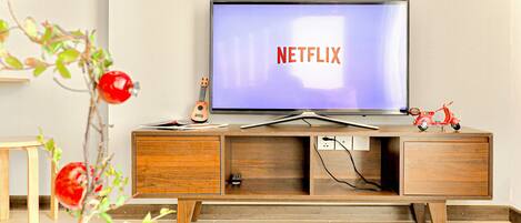 A modern living room with a wooden TV stand, a flat-screen TV displaying the Netflix logo, and a small plant with red berries.