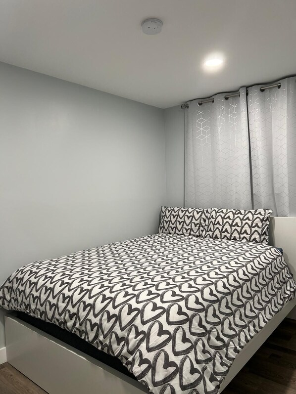 Un dormitorio con cama, cortinas grises y una lámpara de techo.