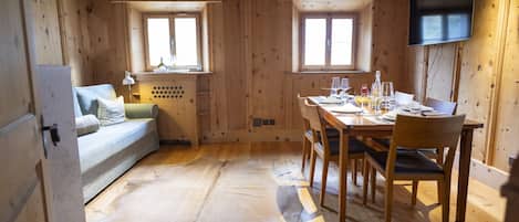 A cozy cabin with a wooden interior, a dining table set for four, a sofa, and a TV mounted on the wall.