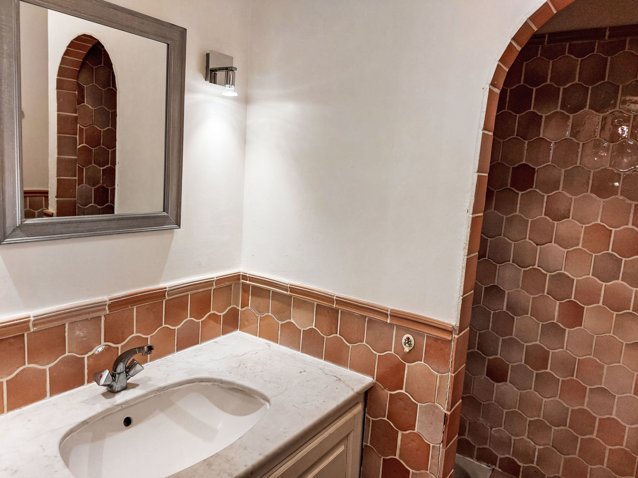 A bathroom with a white sink, a mirror, and a shower with a tiled wall.
