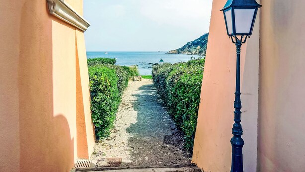 Un sendero conduce a una vista costera, enmarcado por un arco de ladrillo y un farol.