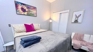 Ein Schlafzimmer mit einem Bett, einem Sessel, einer Tür und einer Wand mit zwei gerahmten Bildern.