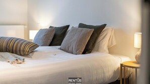 A neatly made bed with pillows, a bedside lamp, and a small table.