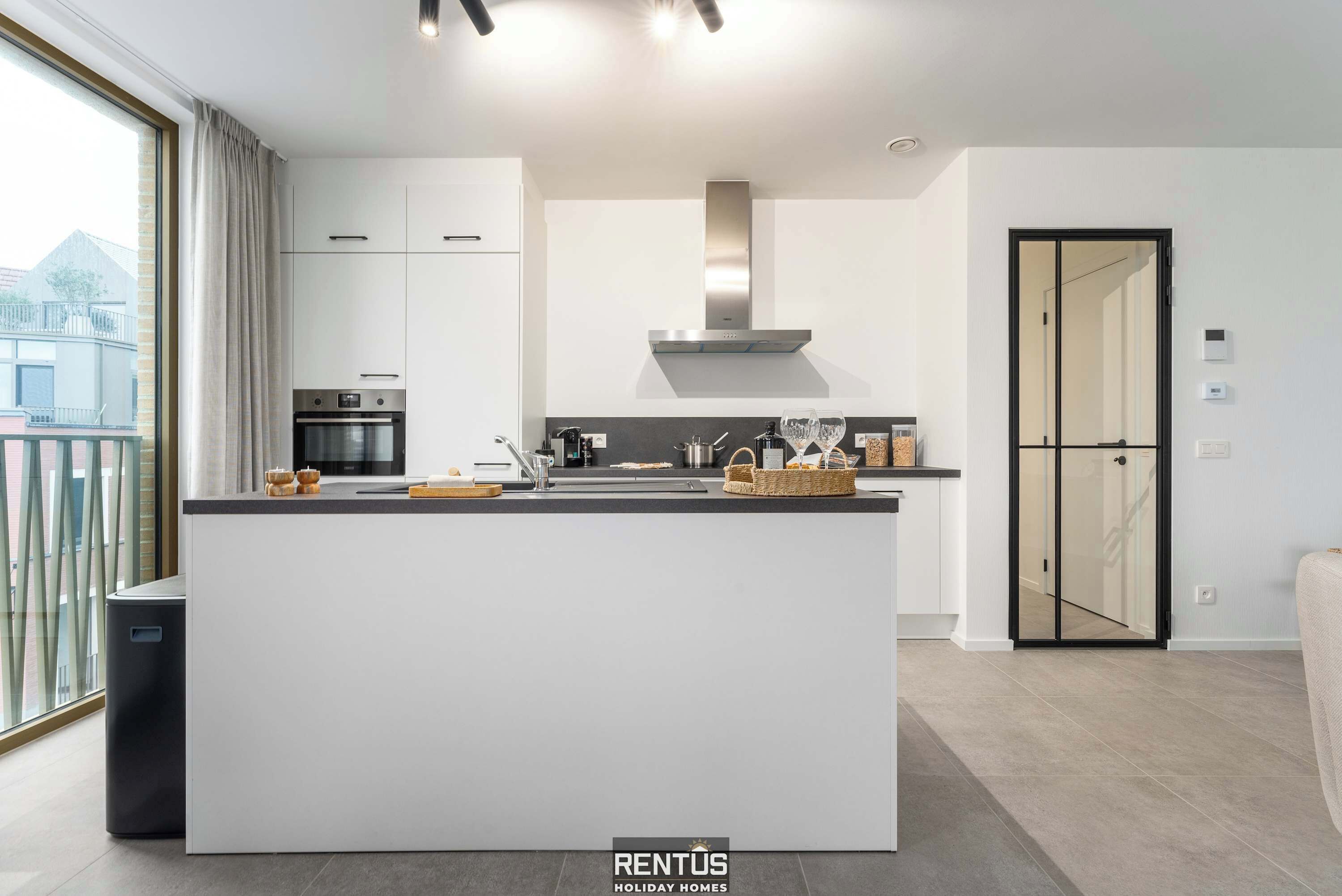 A modern kitchen with a central island, stainless steel appliances, and a large window offering a view of the city.