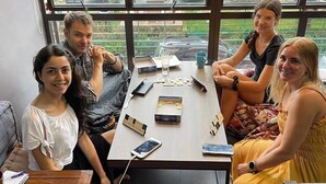 A group of people seated around a table with a window view, a laptop, and some personal items on the table. - Bricks Cameron Hostel (Tanah Rata)
