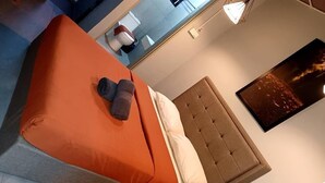A hotel room with a bed, a headboard, a wall-mounted TV, and a painting. - Bricks Cameron Hostel (Tanah Rata)