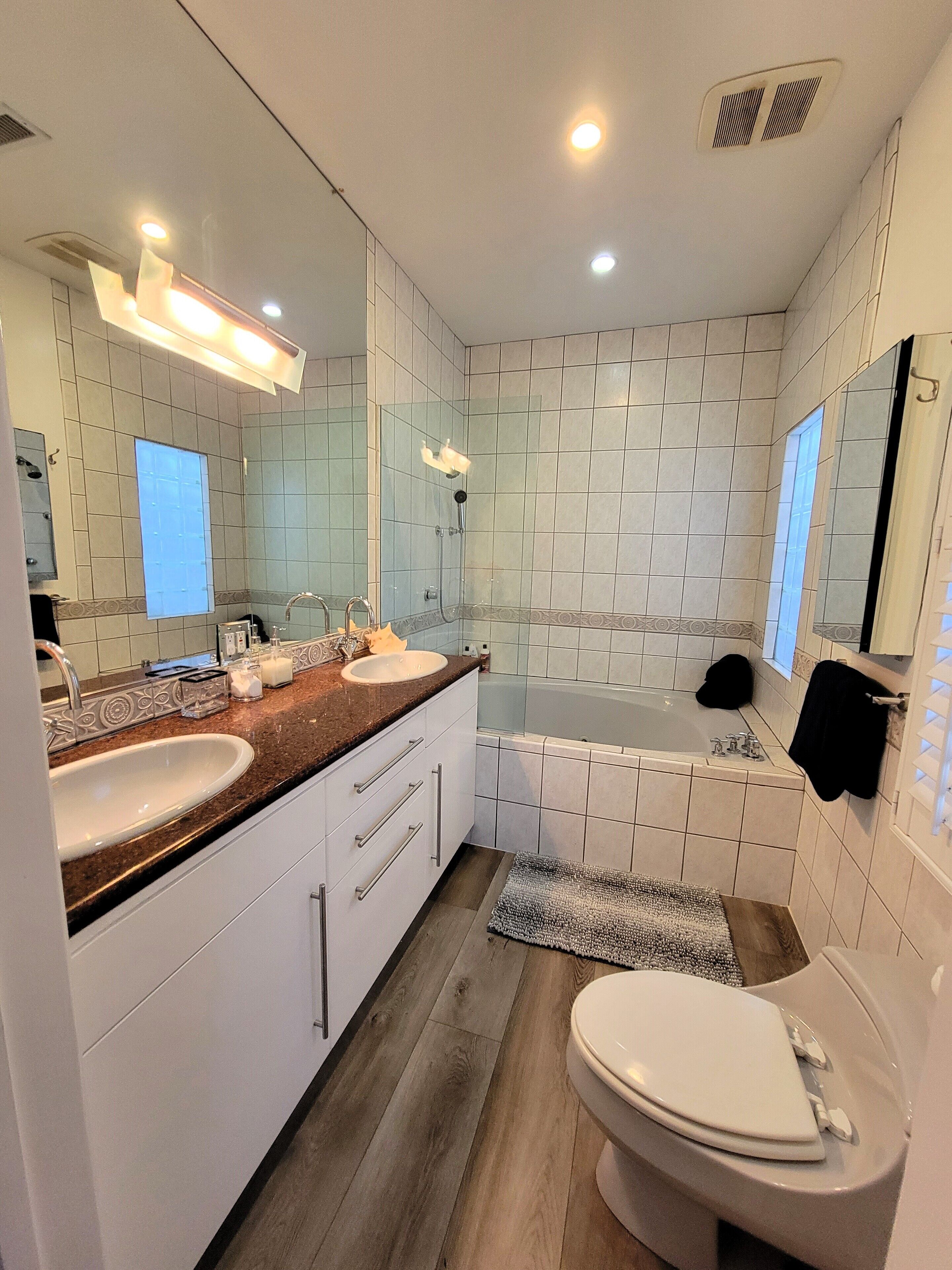 Un baño moderno con un espejo grande, dos lavamanos, una bañera y un inodoro.