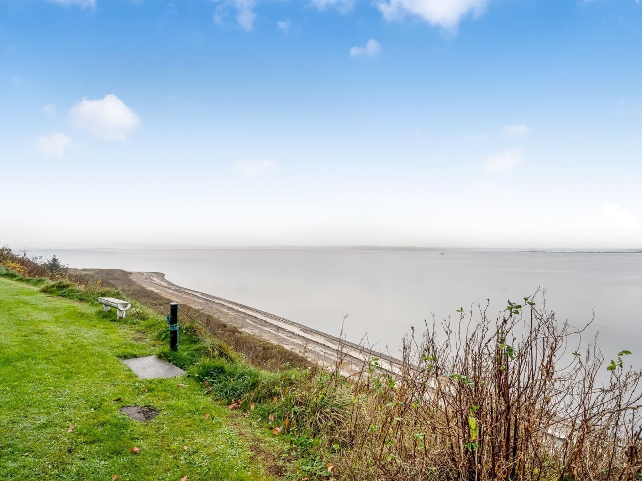 A coastal landscape with a grassy path, a bench, and a view of the sea.