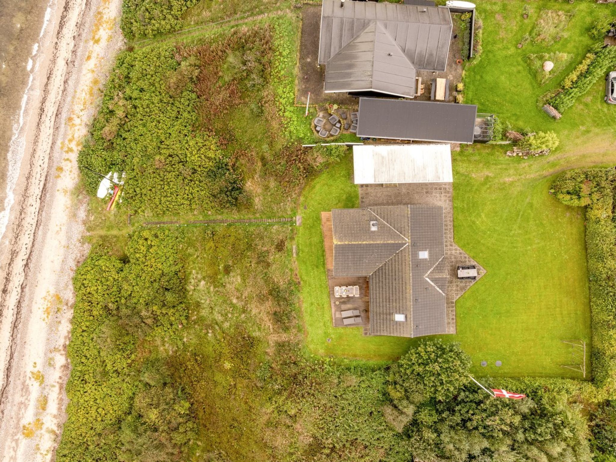 An aerial view of a residential property with a large house, a smaller attached structure, and a well-maintained lawn.