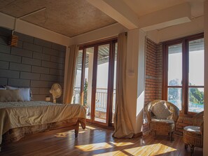 A bedroom with a bed, a fan, and a view of the outdoors through a large window. - Hills Tale Backpackers Hostel (Kalimpong)