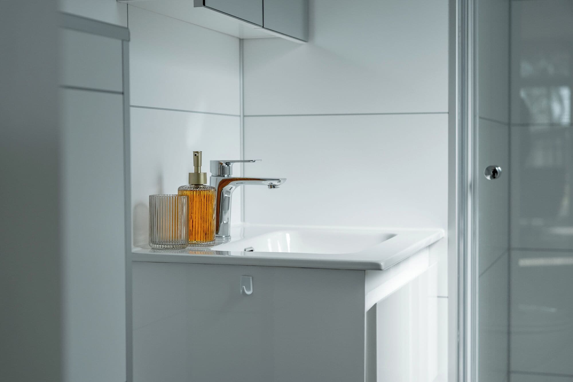 A bathroom with a white sink, a glass container with a spray bottle, and a cabinet.