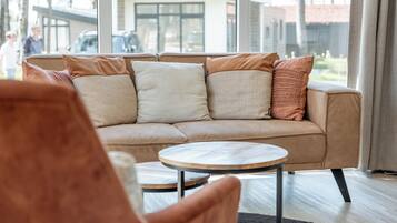 Una sala de estar moderna con un sofá color beige, una mesa de centro redonda de madera y un ventanal con vistas a una zona residencial.
