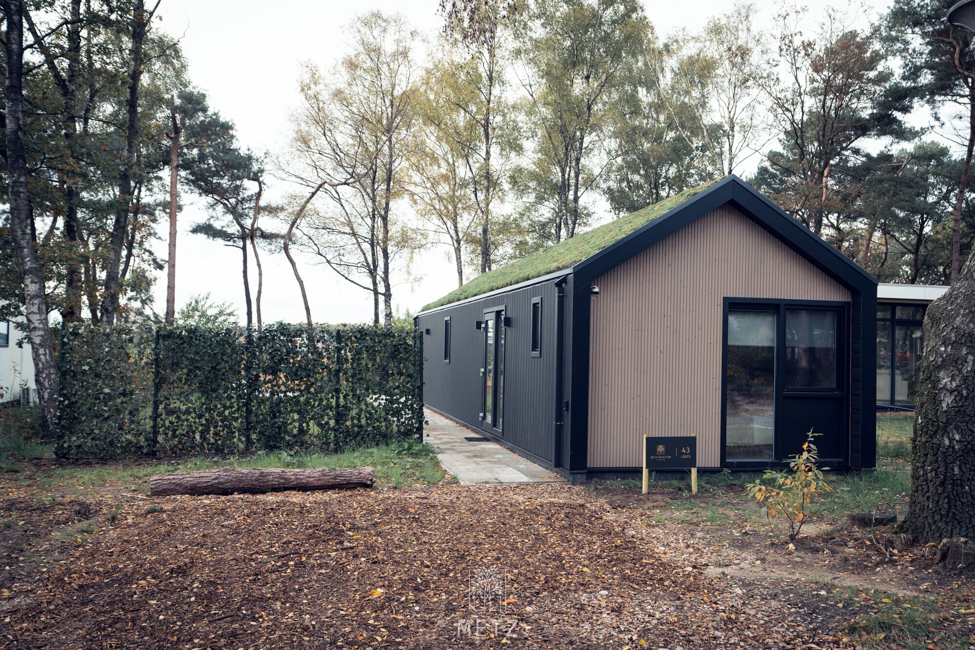 A modern, single-story building with a sloped roof, large windows, and a small porch area.