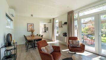 A modern living room with a dining area, large windows, and a view of the outdoors.
