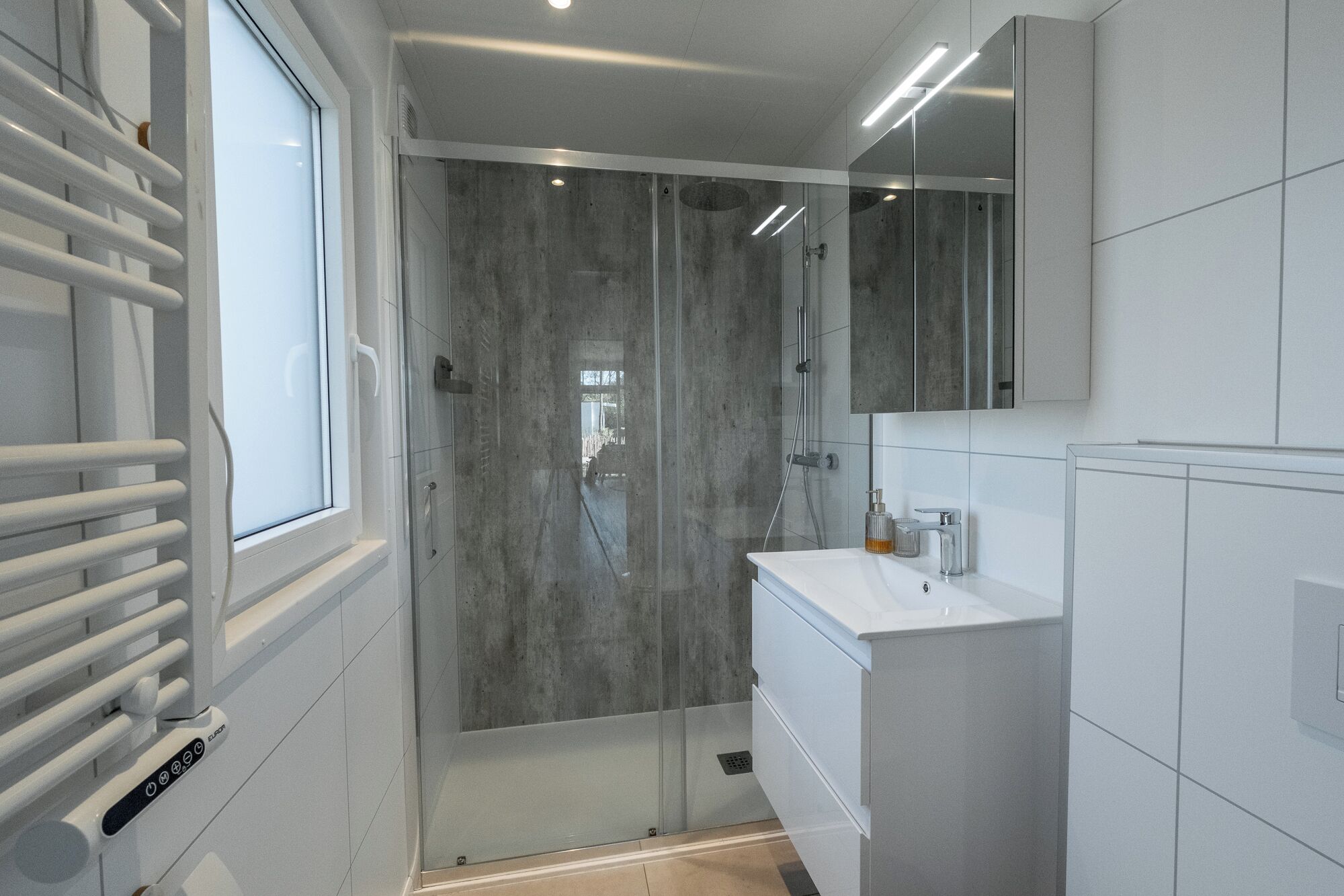 A modern bathroom with a glass shower enclosure, a white sink, and a mirror above the vanity.