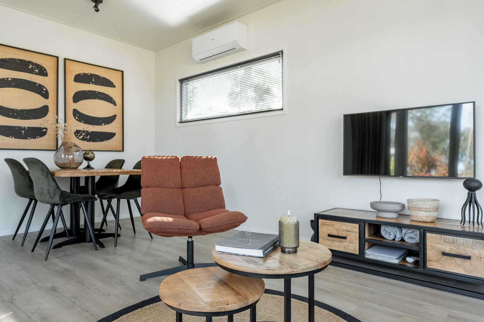Un salon moderne avec un canapé, une table basse ronde, un téléviseur et des œuvres d’art accrochées au mur.