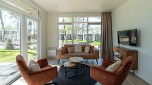 Un salon moderne comprenant un canapé, deux fauteuils, une table basse, un téléviseur et de grandes fenêtres.