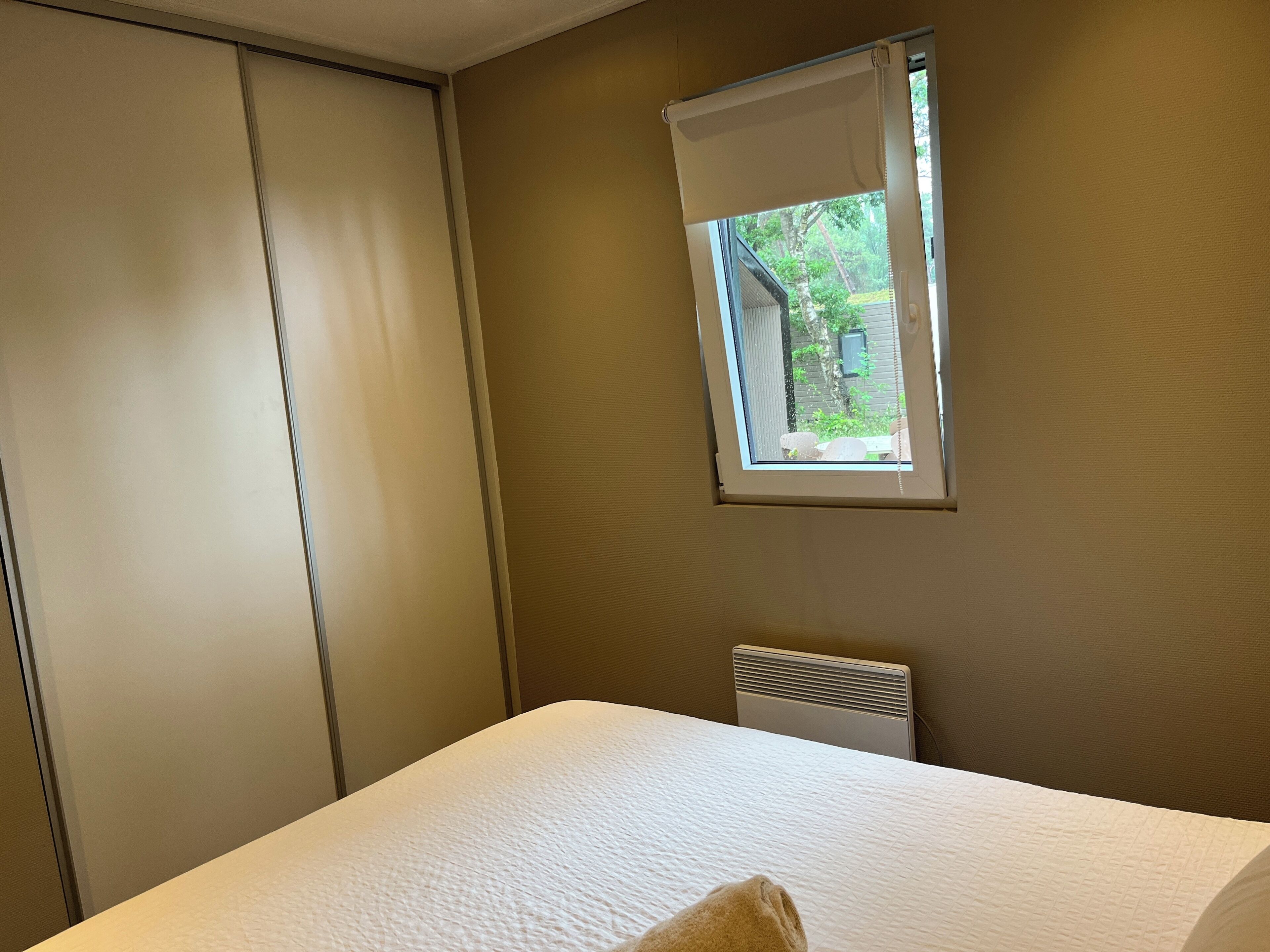 A bedroom with a bed, a window with a view of greenery, a radiator, and a sliding door.