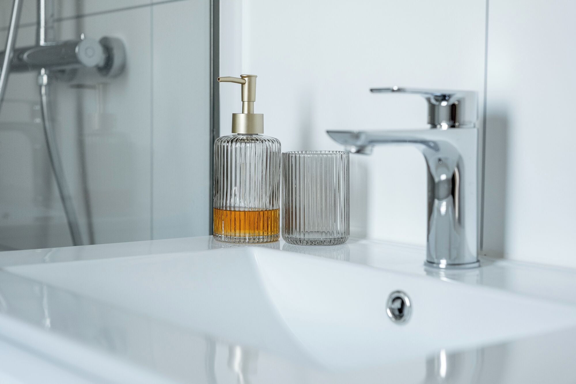 Un baño con un lavabo blanco, una botella de vidrio con dispensador de bomba y un vaso de vidrio.