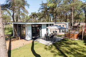 A modern outdoor patio with a table and chairs, surrounded by a wooden fence and trees. - Wellness Lodge Hottub  (Haarle)