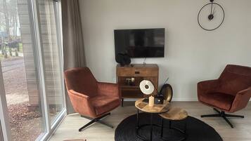A modern living room with two brown armchairs, a wooden coffee table, a black rug, and a TV mounted on the wall.