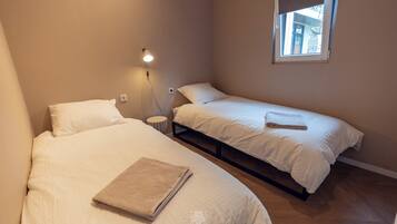 A small, cozy room with two beds, a bedside table, and a window with a view.