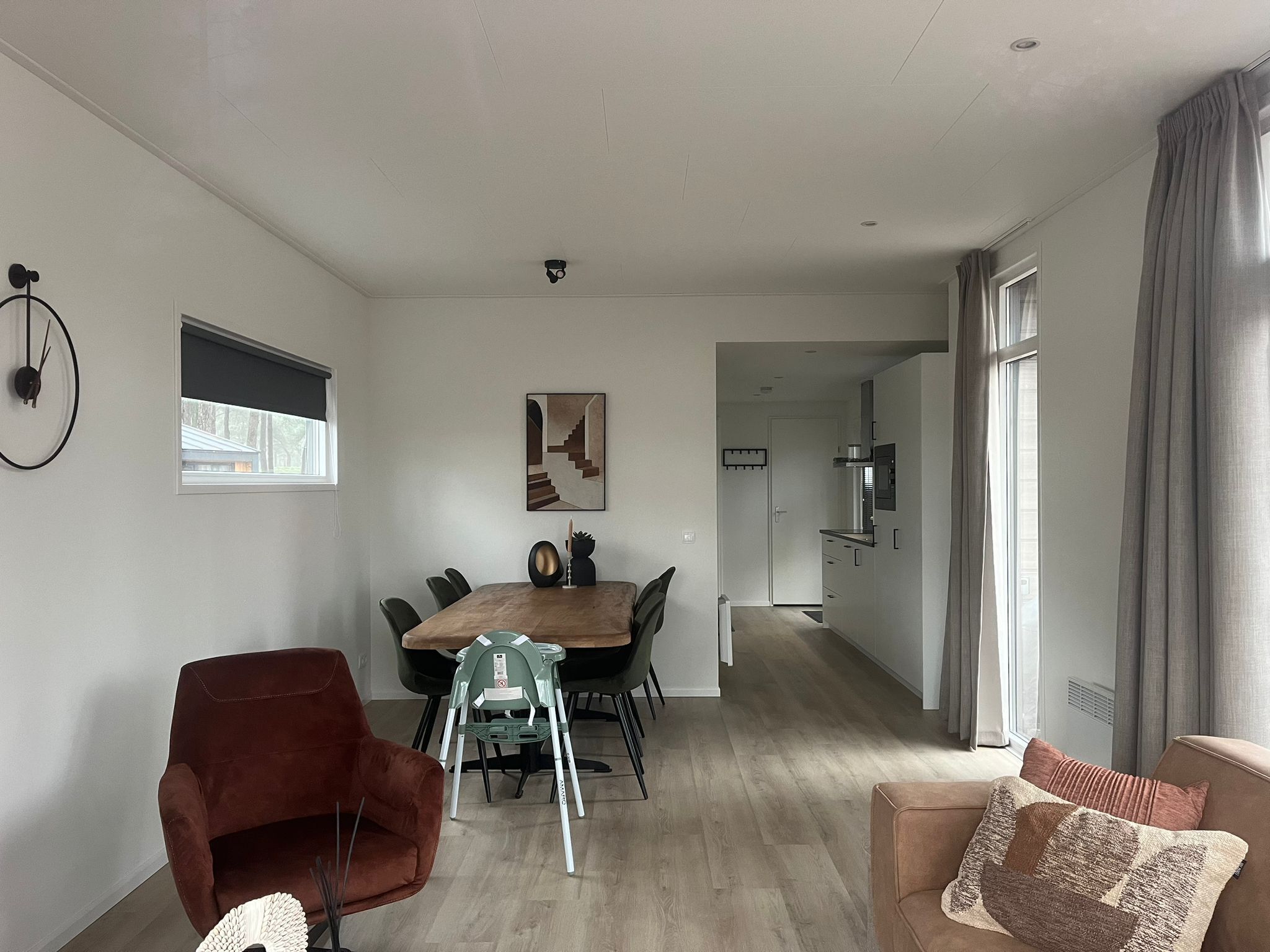 A modern living room with a dining table, chairs, a sofa, and a kitchen area in the background.