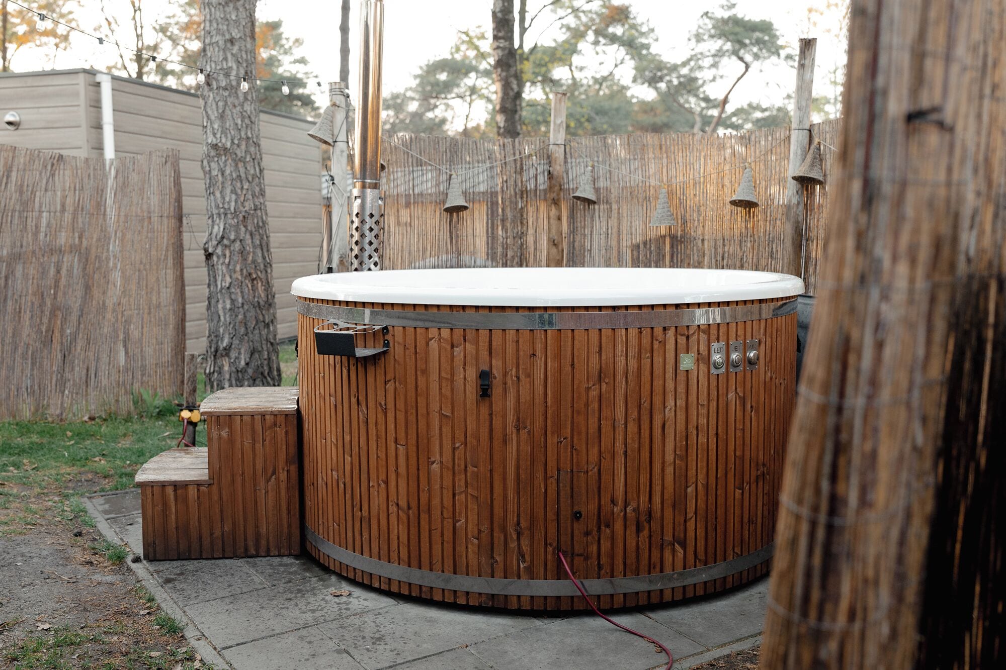 Un bain à remous en bois, doté d’un couvercle blanc, d’un panneau de commande avec des boutons et d’un petit banc en bois.