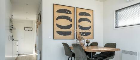 A dining area with a round wooden table, four grey chairs, and two large abstract paintings on the wall.