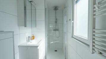 Un baño moderno con ducha de vidrio, un lavamanos blanco y un ventanal amplio.