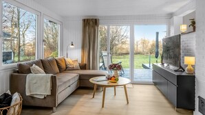 Een moderne woonkamer met een bank, een ronde salontafel met fruit, en een keukenhoek met een televisie en kasten.
