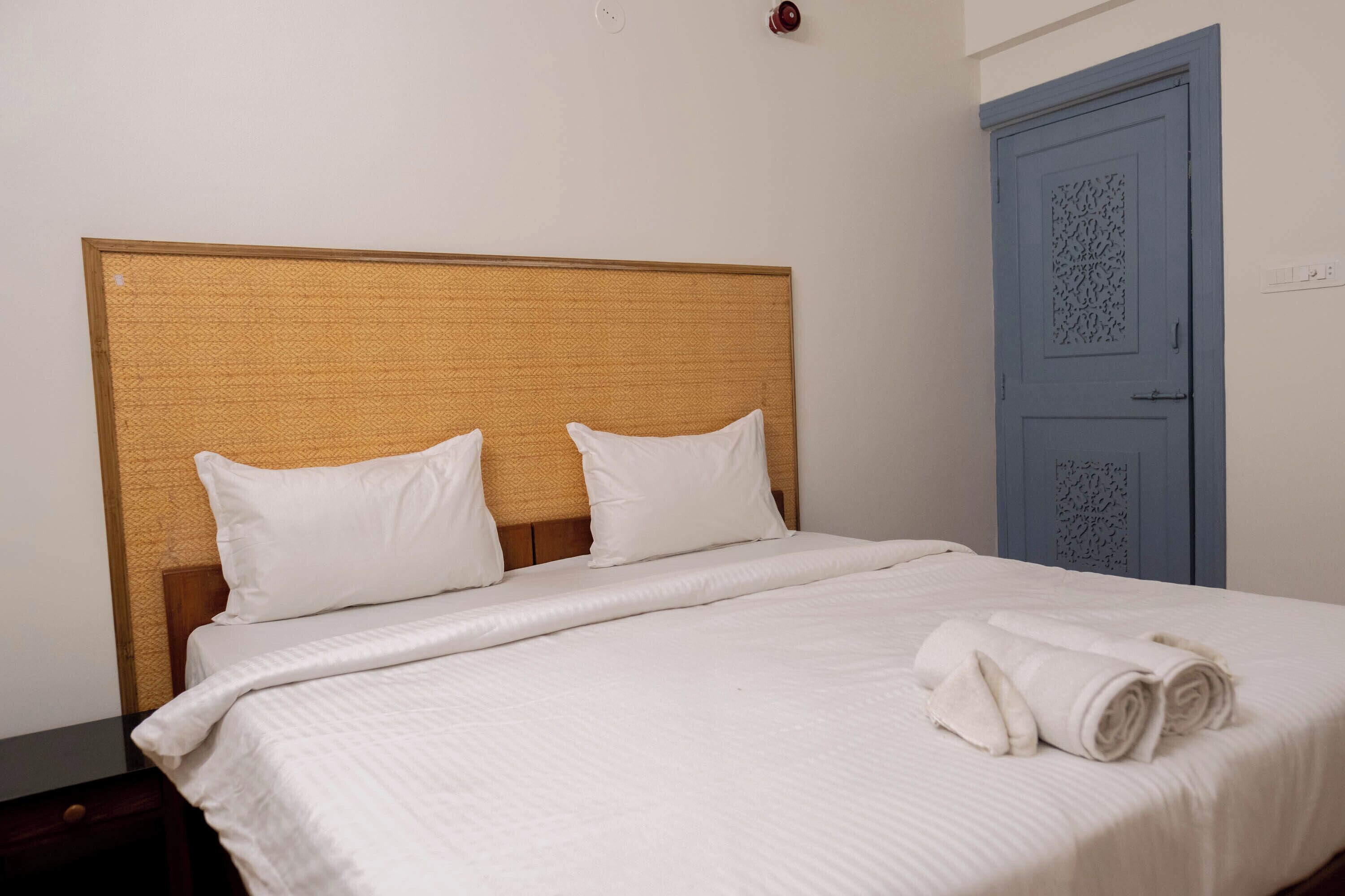 Un letto rifatto con lenzuola e cuscini bianchi, una testiera in legno e una porta blu sullo sfondo.